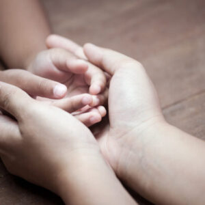 Child Protection - a woman holds a childs hands in hers