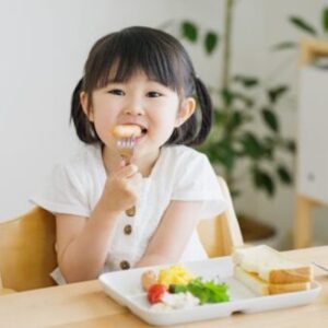 Young girl with black hair and pigtails eats vegetables